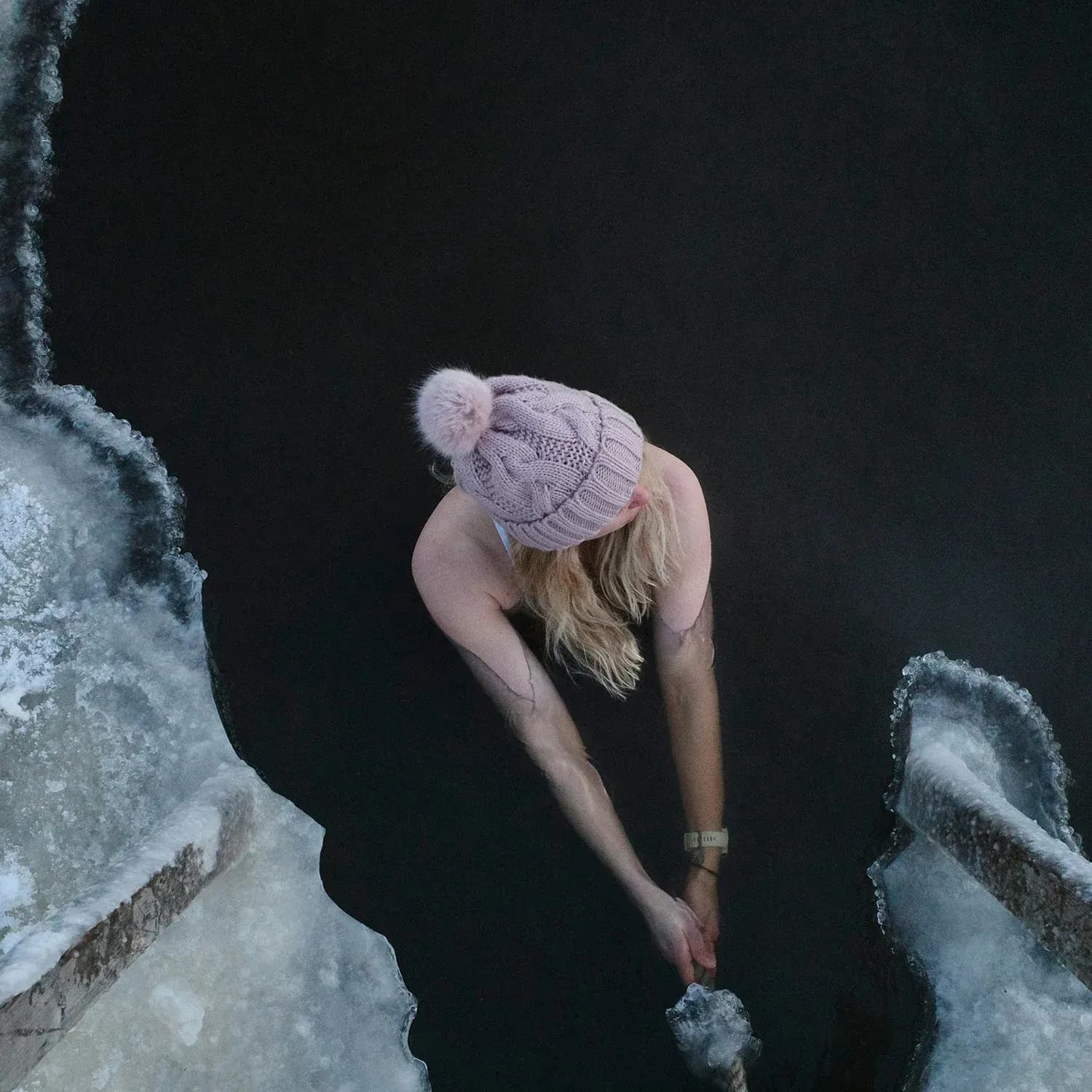 A guest in a knitted hat at the edge of an ice-hole plunge pool after the sauna
